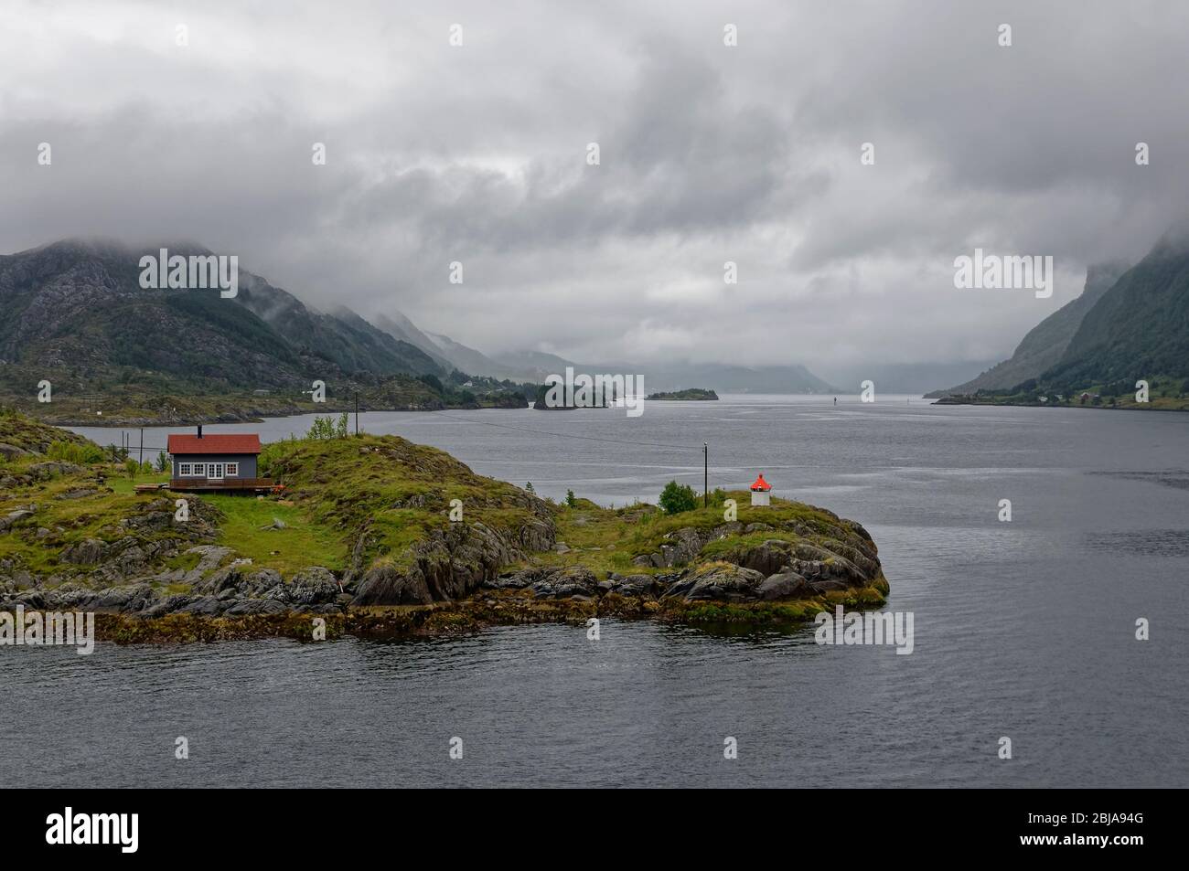 A Norwegian Cabin and Lighthouse on a small Island in the middle of a Fjord on a wet, overcast day with low cloud in late Summer. Stock Photo