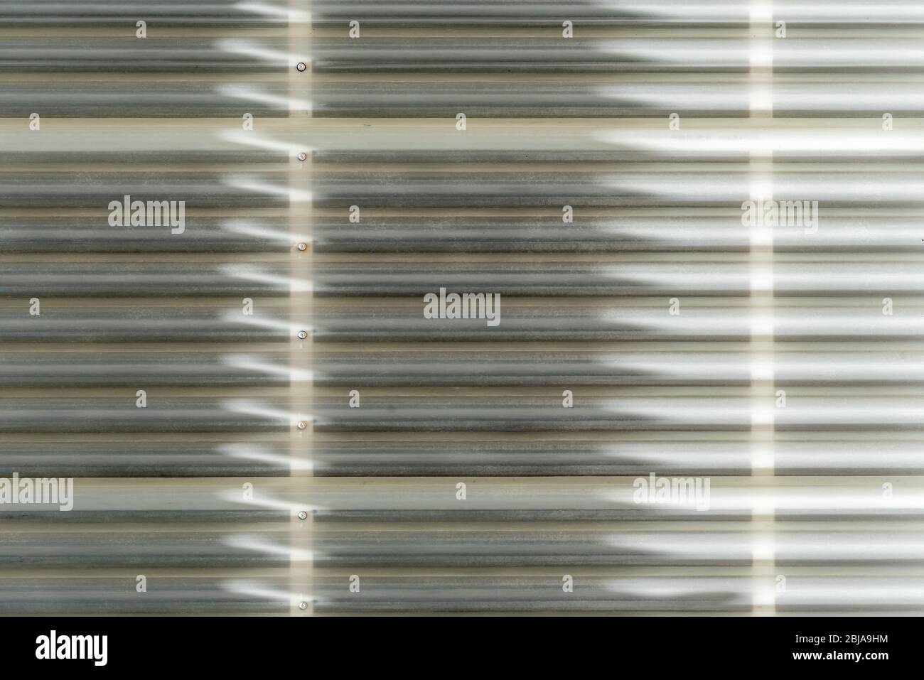 Shadow and light form linear and arrow abstract patterns as sunlight hits exterior plastic cladding on a wall in Australia Stock Photo