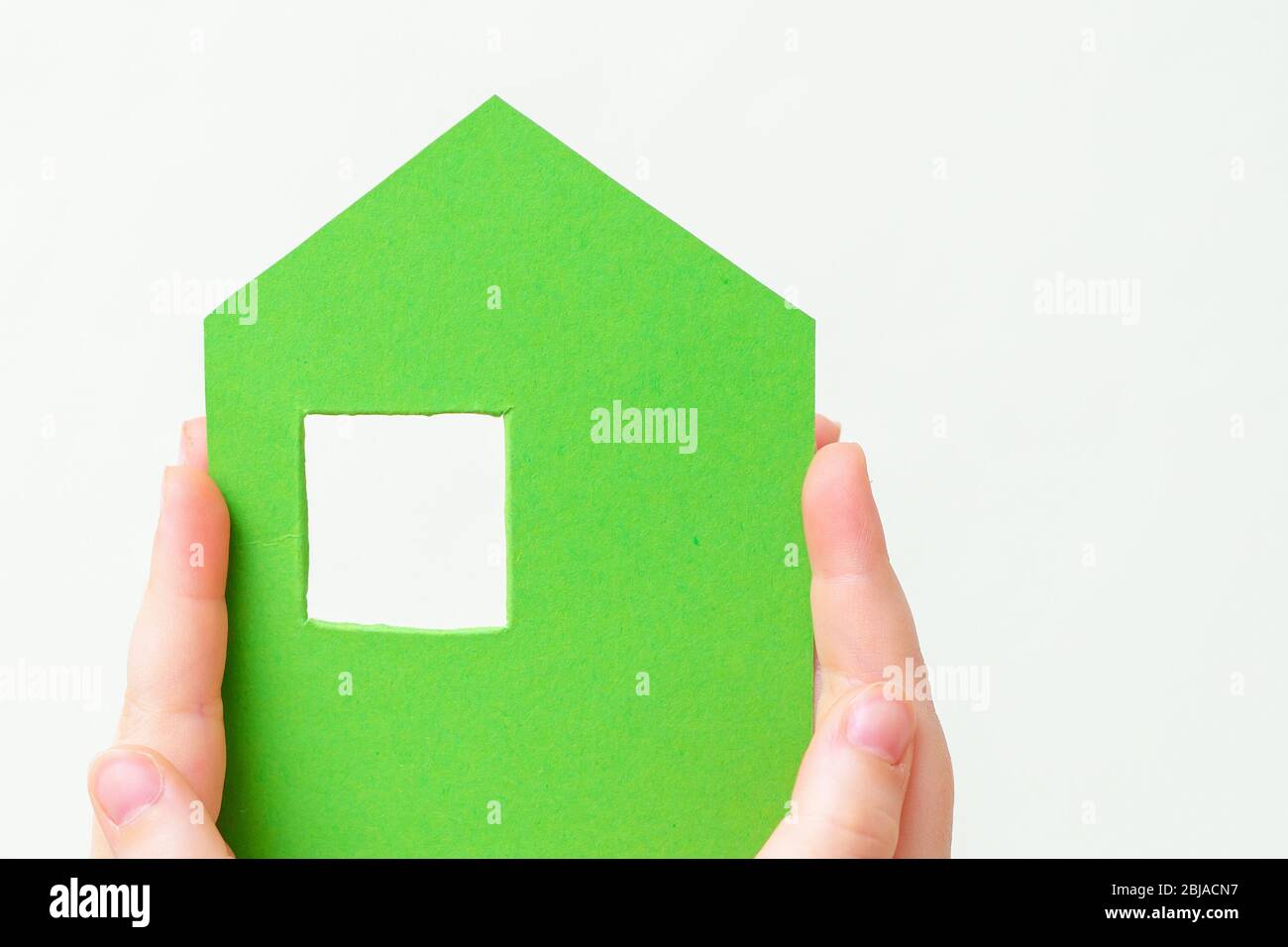 Children's hands holding a green paper house on a white background. Stock Photo