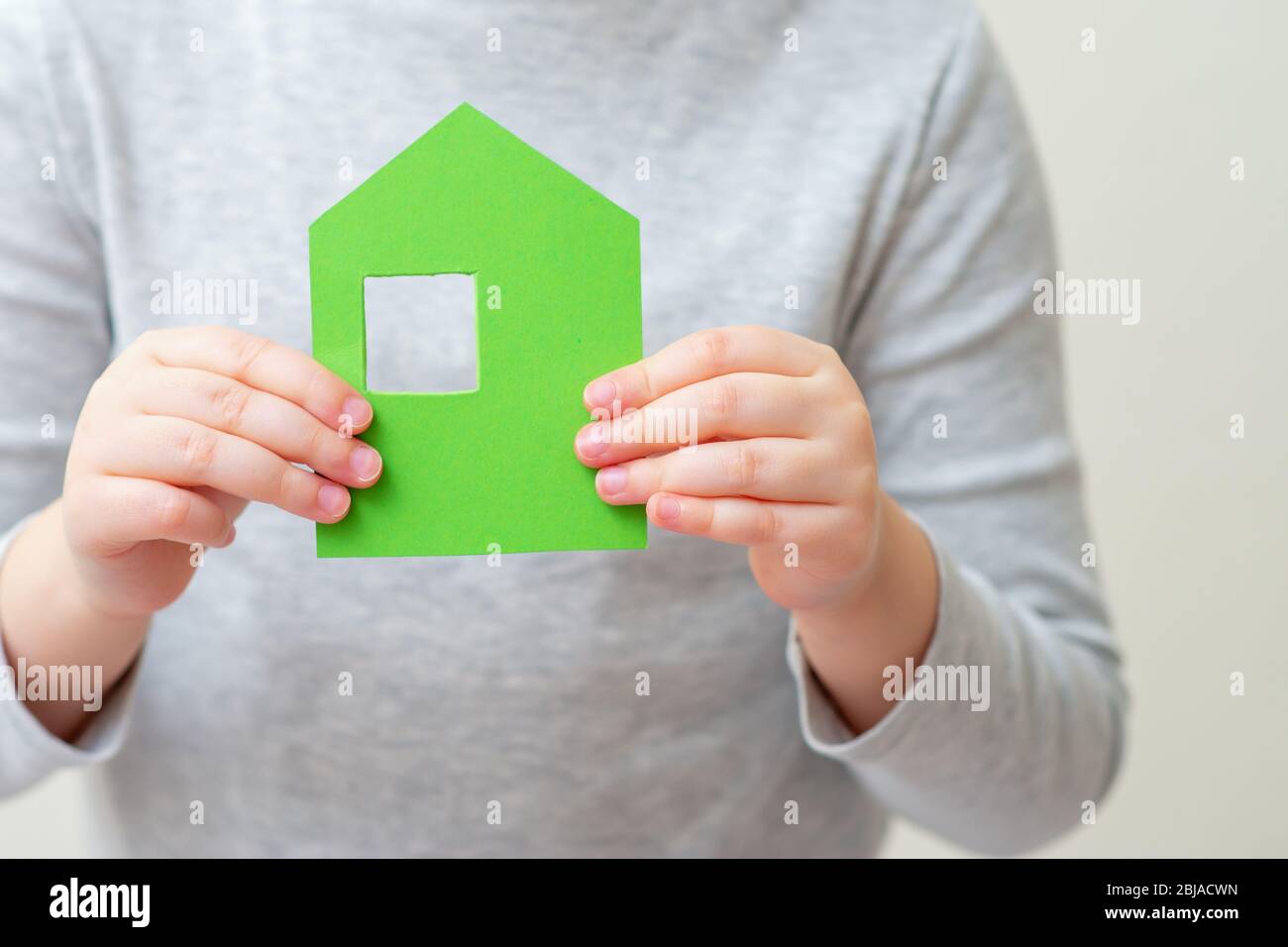 Little paper house in child's hands holding in front of herself. Family home concept. Stock Photo