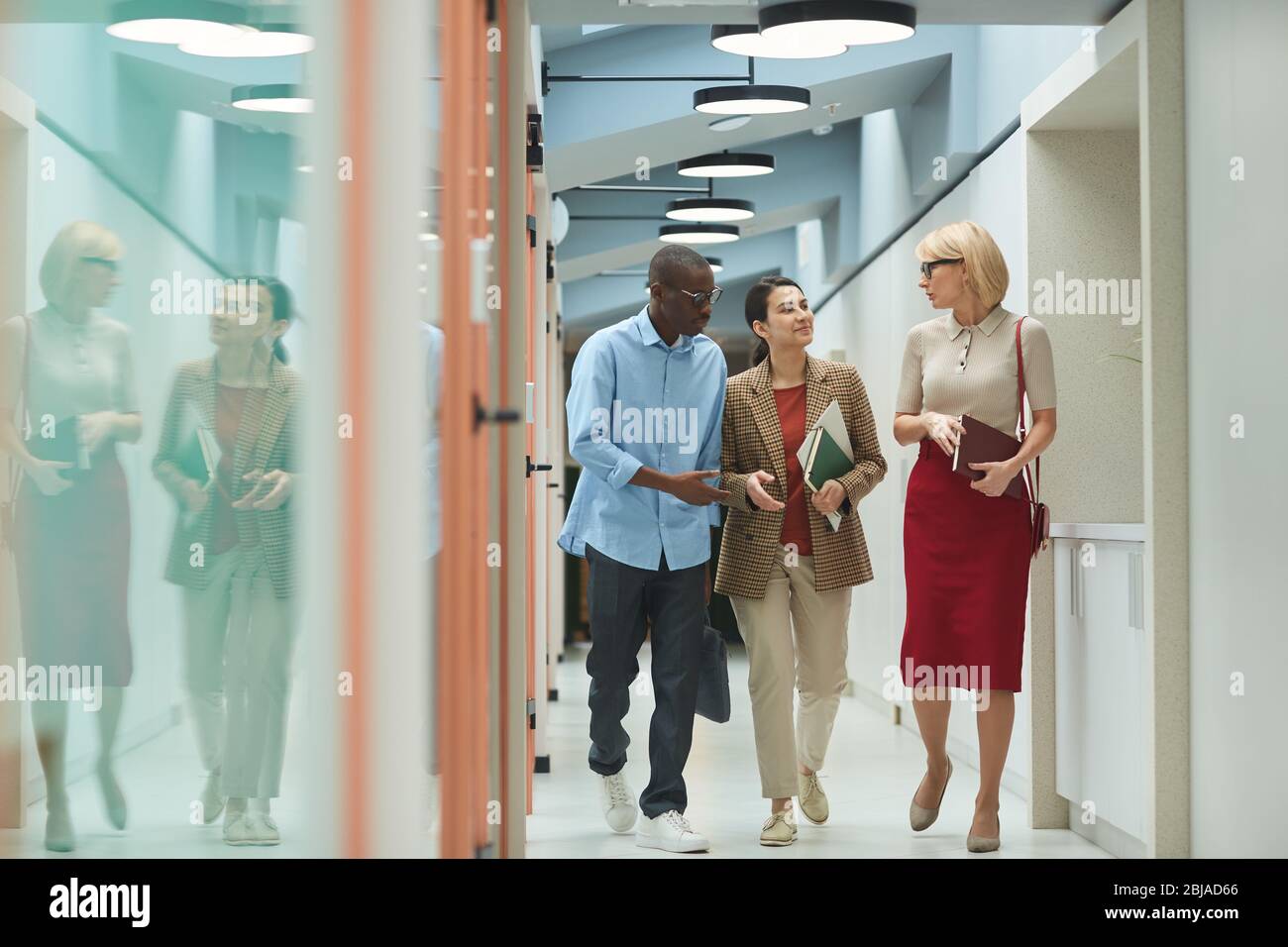 Group of colleagues with documents talking to each other while working along the office corridor Stock Photo