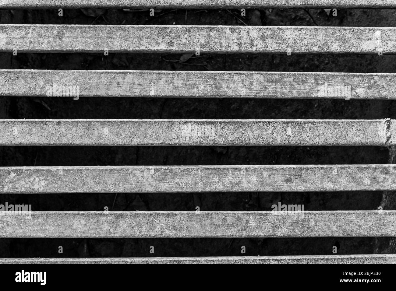 Black and white photo of an iron grate over a drainage channel on the road. Rusty texture on metal. Horizontal. Stock Photo