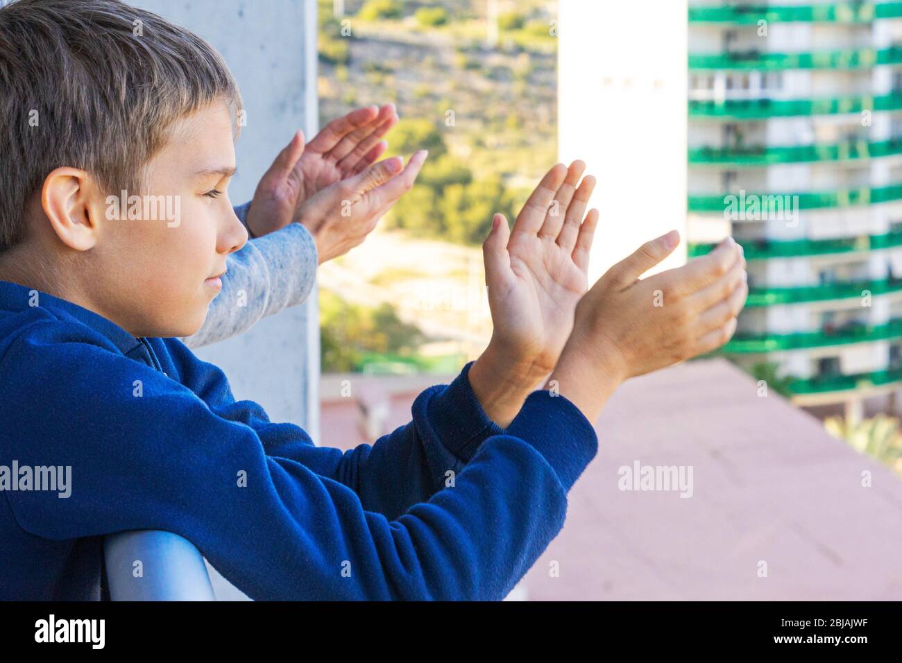 Family applauding medical staff from balcony. People clapping on balconies and windows in support of health workers during the Coronavirus pandemic Stock Photo