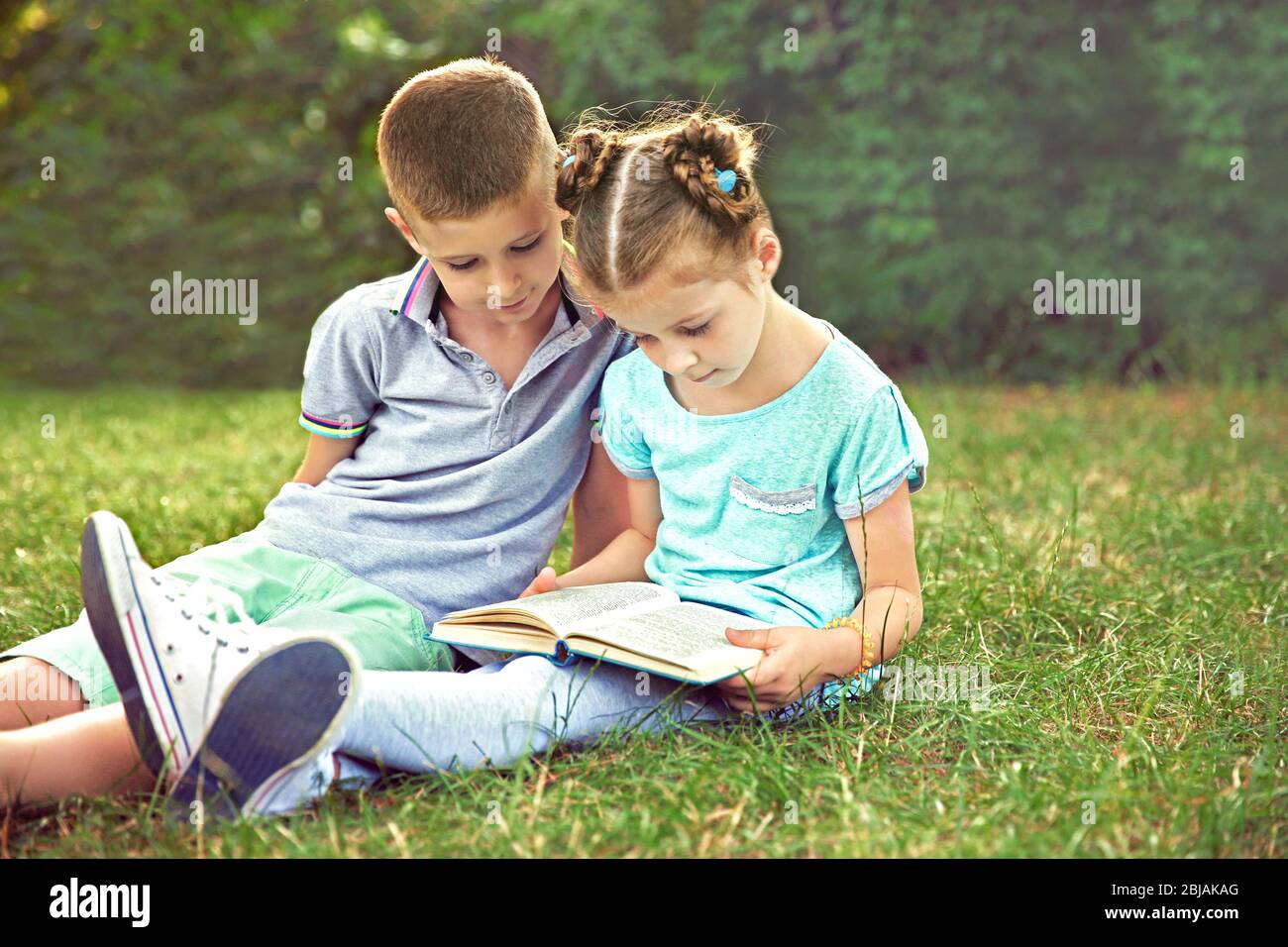 Cute boy and girl reading book in summer park Stock Photo - Alamy