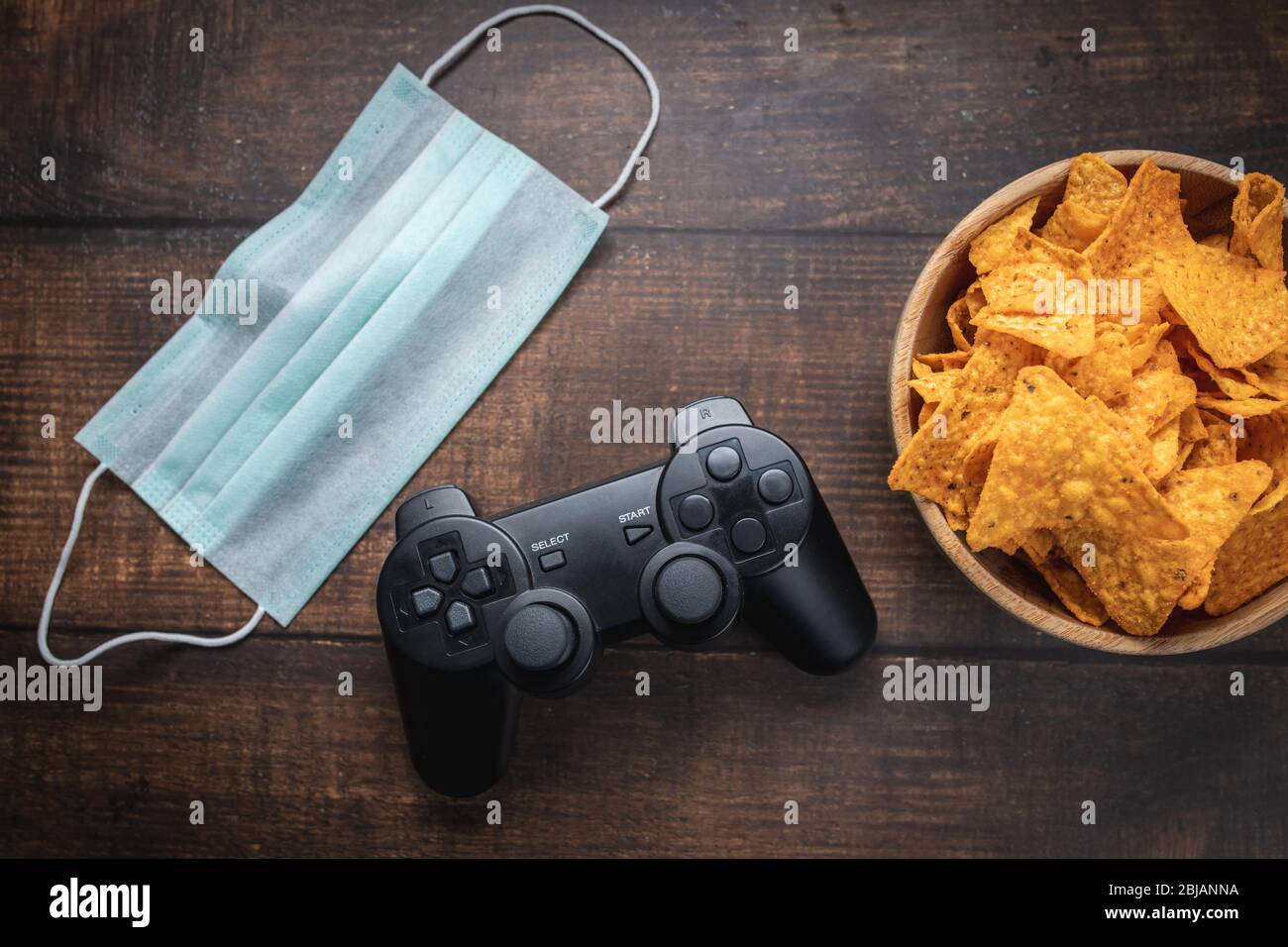 Game console rc, bowl of crisps and medical mask on wooden table. Coronavirus Covid-19 quarantine stay at home concept. Stock Photo