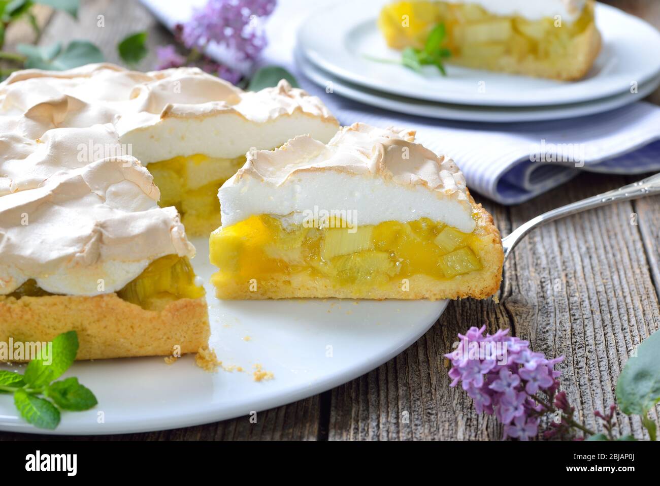 Delicious rhubarb cake topped with sweet meringue served on a wooden table with springlike lilac decoration Stock Photo