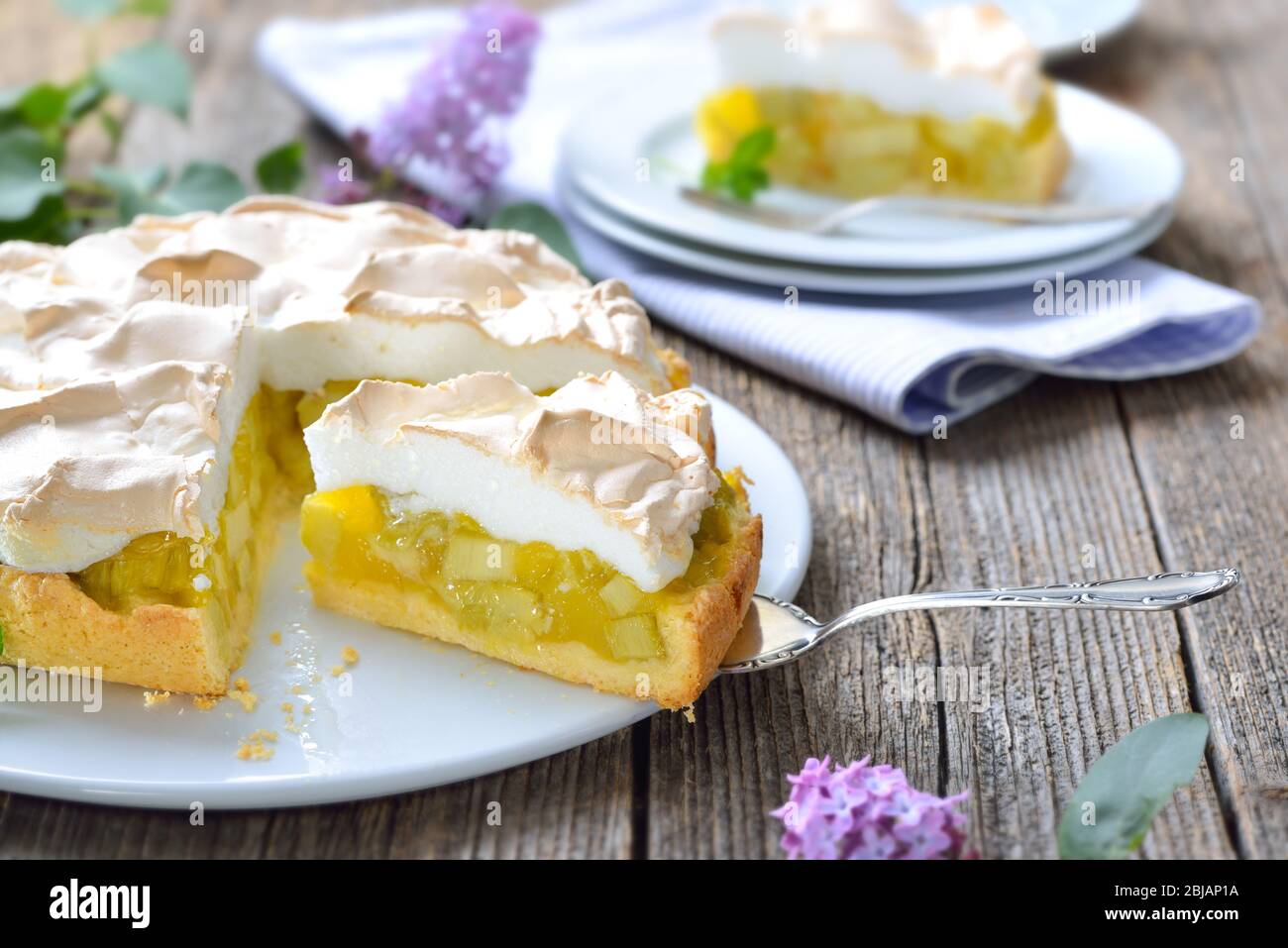 Delicious rhubarb cake topped with sweet meringue served on a wooden table with springlike lilac decoration Stock Photo