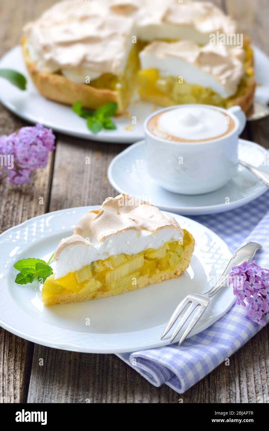 Delicious rhubarb cake topped with sweet meringue and a cup of cappuccino served on a wooden table with springlike lilac decoration Stock Photo