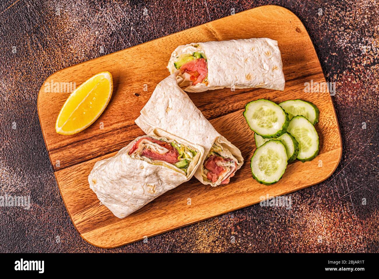 Wrapped sandwich with salmon, lettuce, cucumber and cream cheese, top view. Stock Photo
