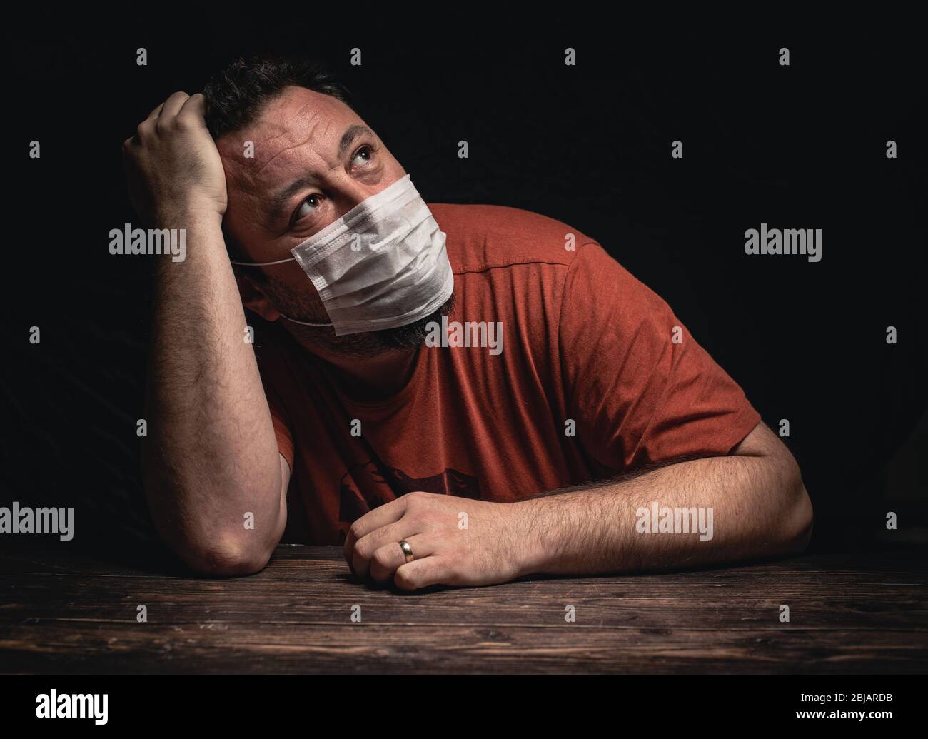 Attractive man with protective medical mask sitting desperate on the table looking worried, depressed, thoughtful and lonely suffering depression beca Stock Photo