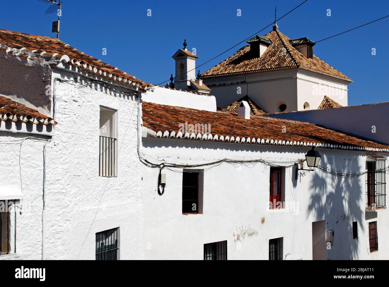 Townhouses with the church (Iglesia de San Jacinto) to the rear,  whitewashed village (pueblo blanco), Macharaviaya, Malaga Province, Spain. Stock Photo