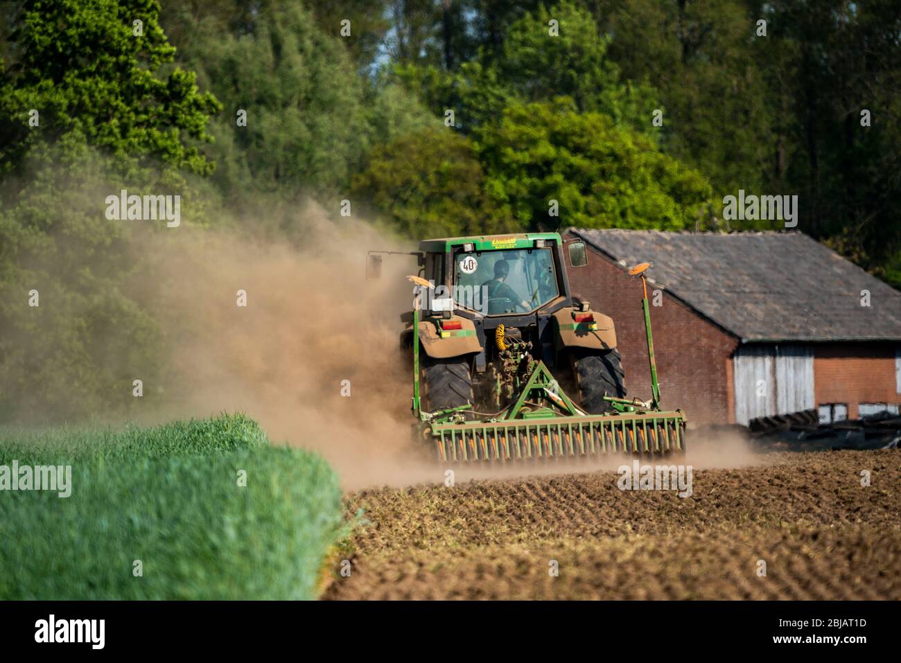 Farmer working the fields in spring, dry April 2020, tractor pulls thick cloud of dust, while cultivating, loosening the soil, behind him, Niederrhein Stock Photo