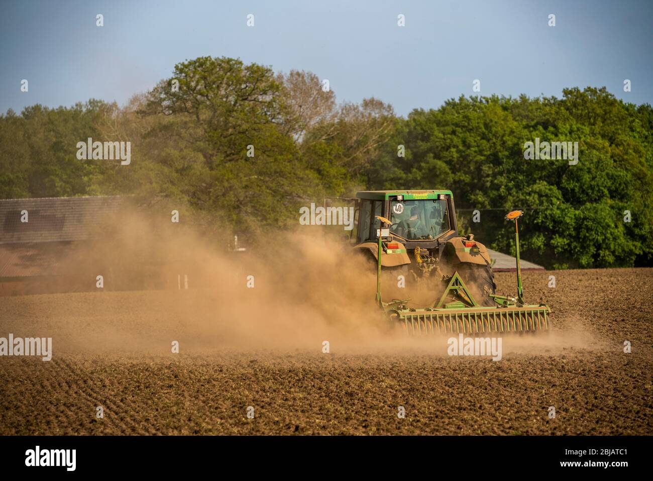 Farmer working the fields in spring, dry April 2020, tractor pulls thick cloud of dust, while cultivating, loosening the soil, behind him, Niederrhein Stock Photo