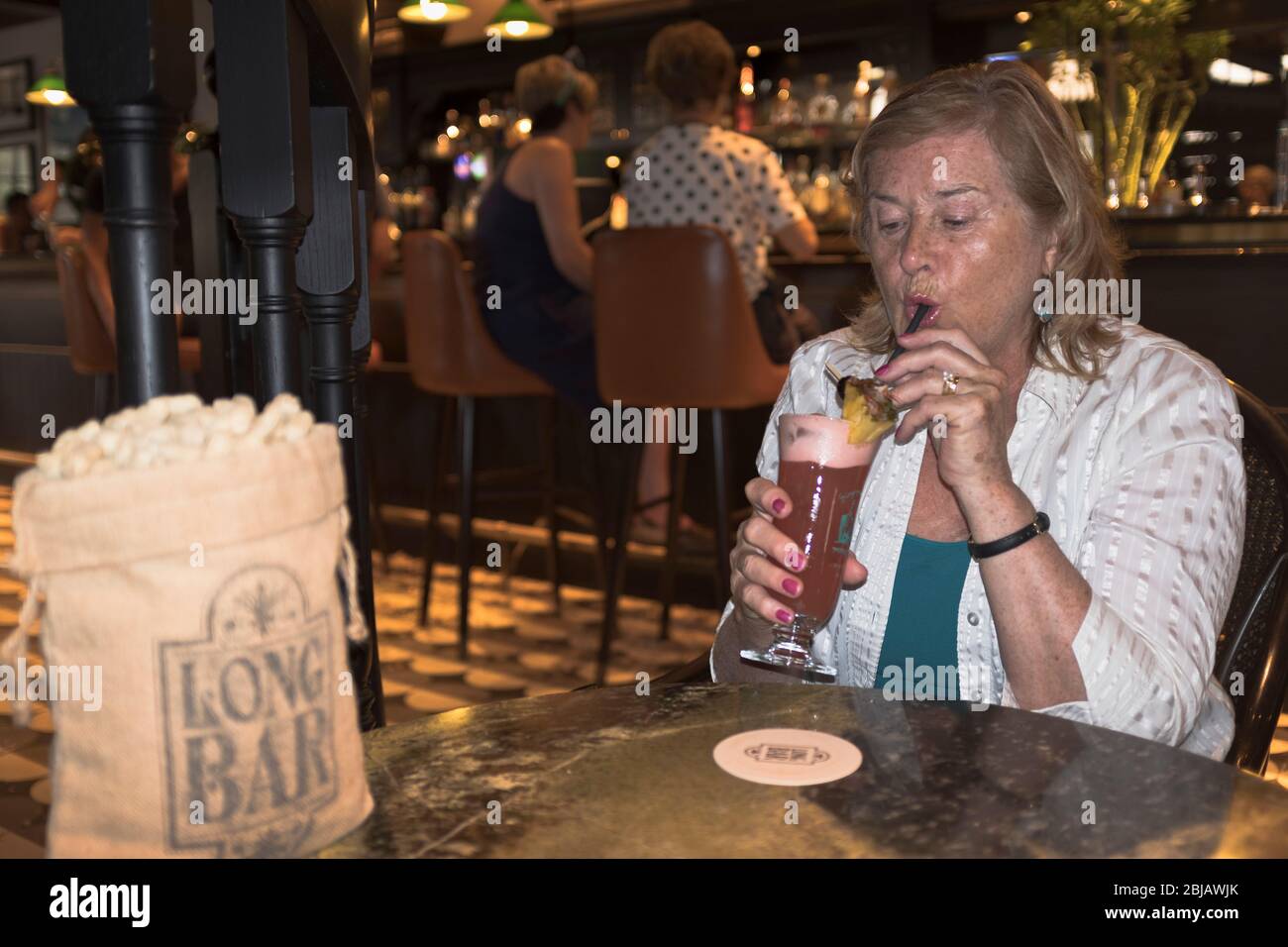 dh Long Bar bag of peanuts RAFFLES HOTEL SINGAPORE Woman tourist drinking a Singapore sling Stock Photo