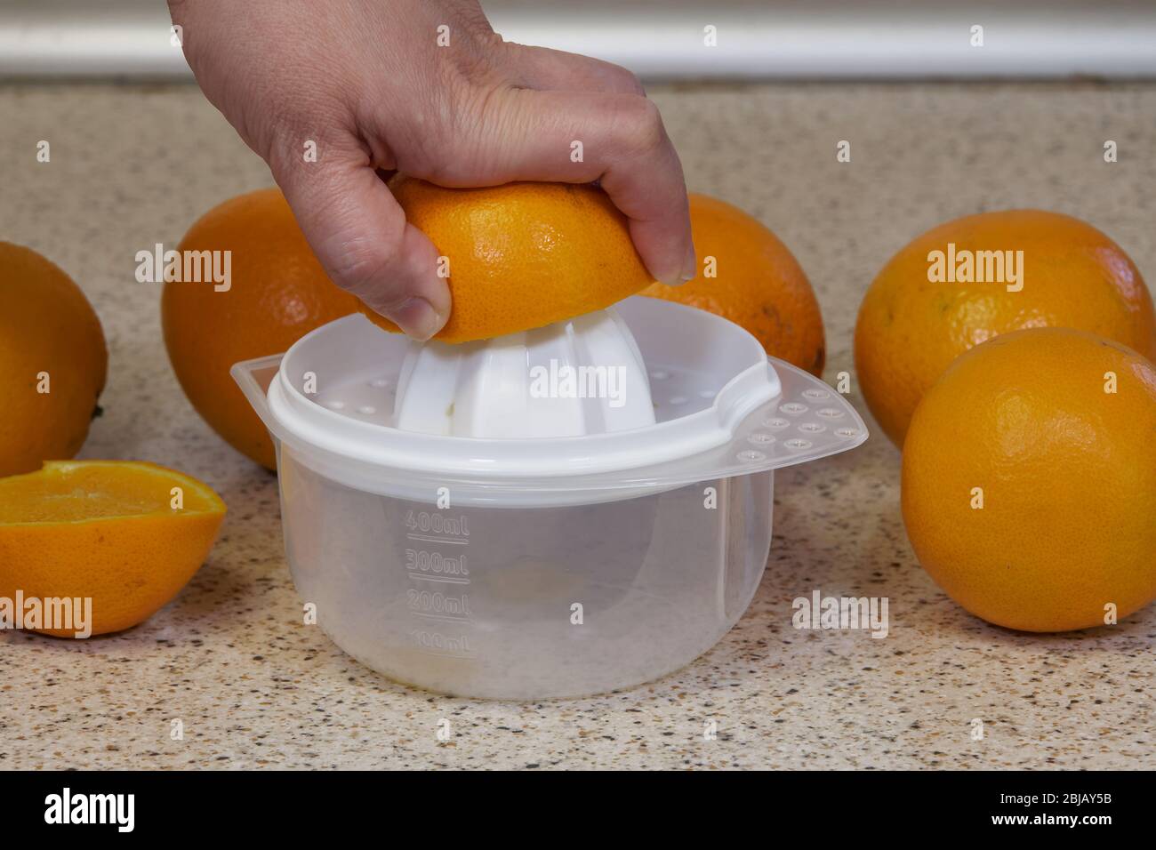 Squeezing orange juice by hand on a plastic squeezer. Female on bench