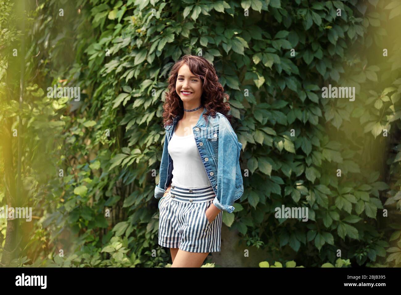 Beautiful young girl posing on green foliage background Stock Photo - Alamy