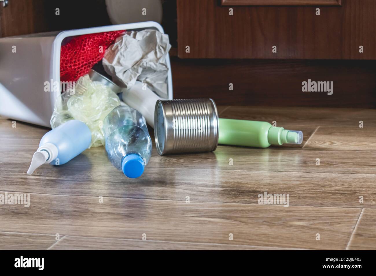 A plastic trash can with garbage lies on the floor near the kitchen ...