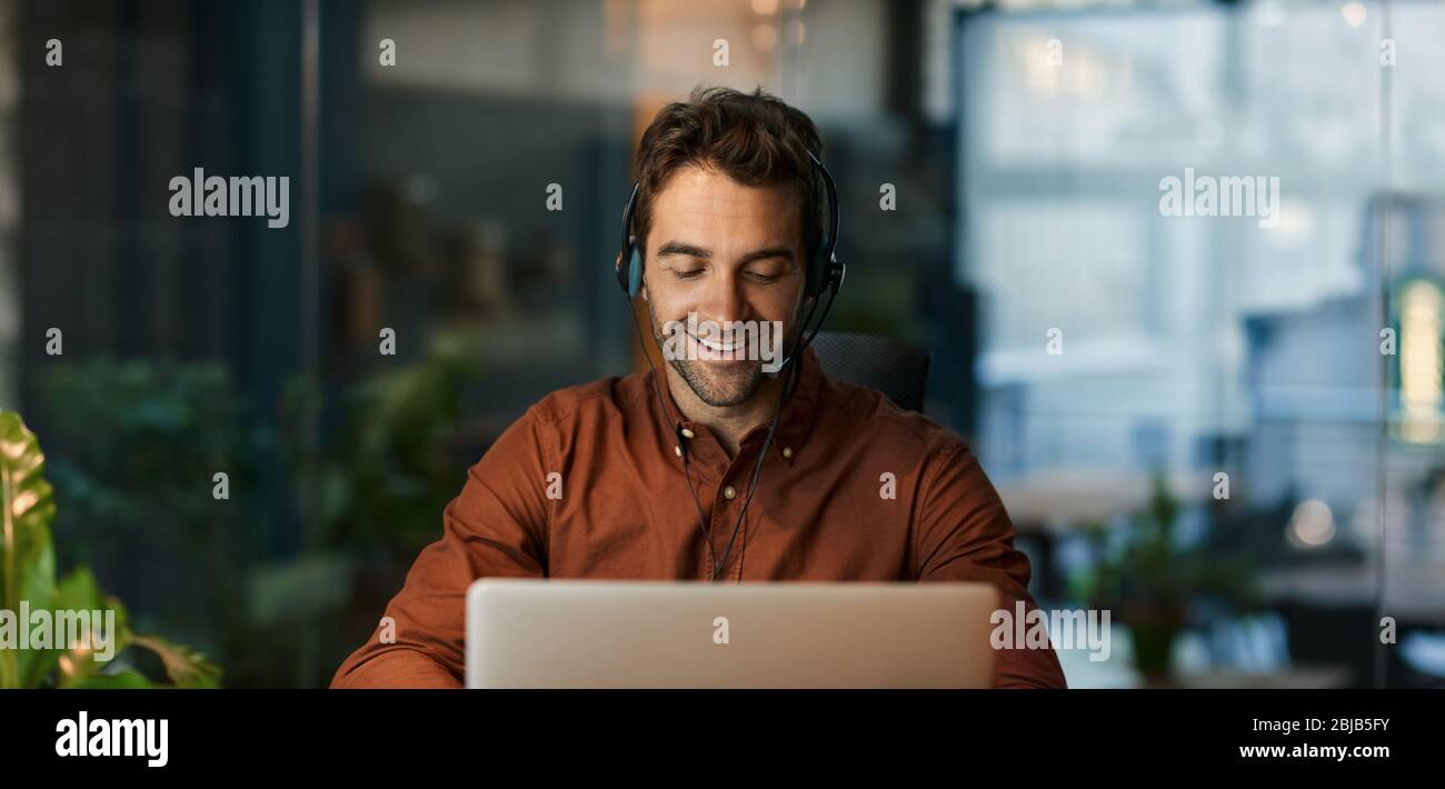 Smiling businessman talking on a headset and using a laptop Stock Photo
