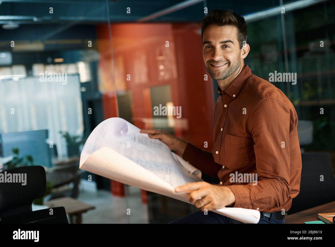 Smiling architect reading blueprints while working late in an office Stock Photo