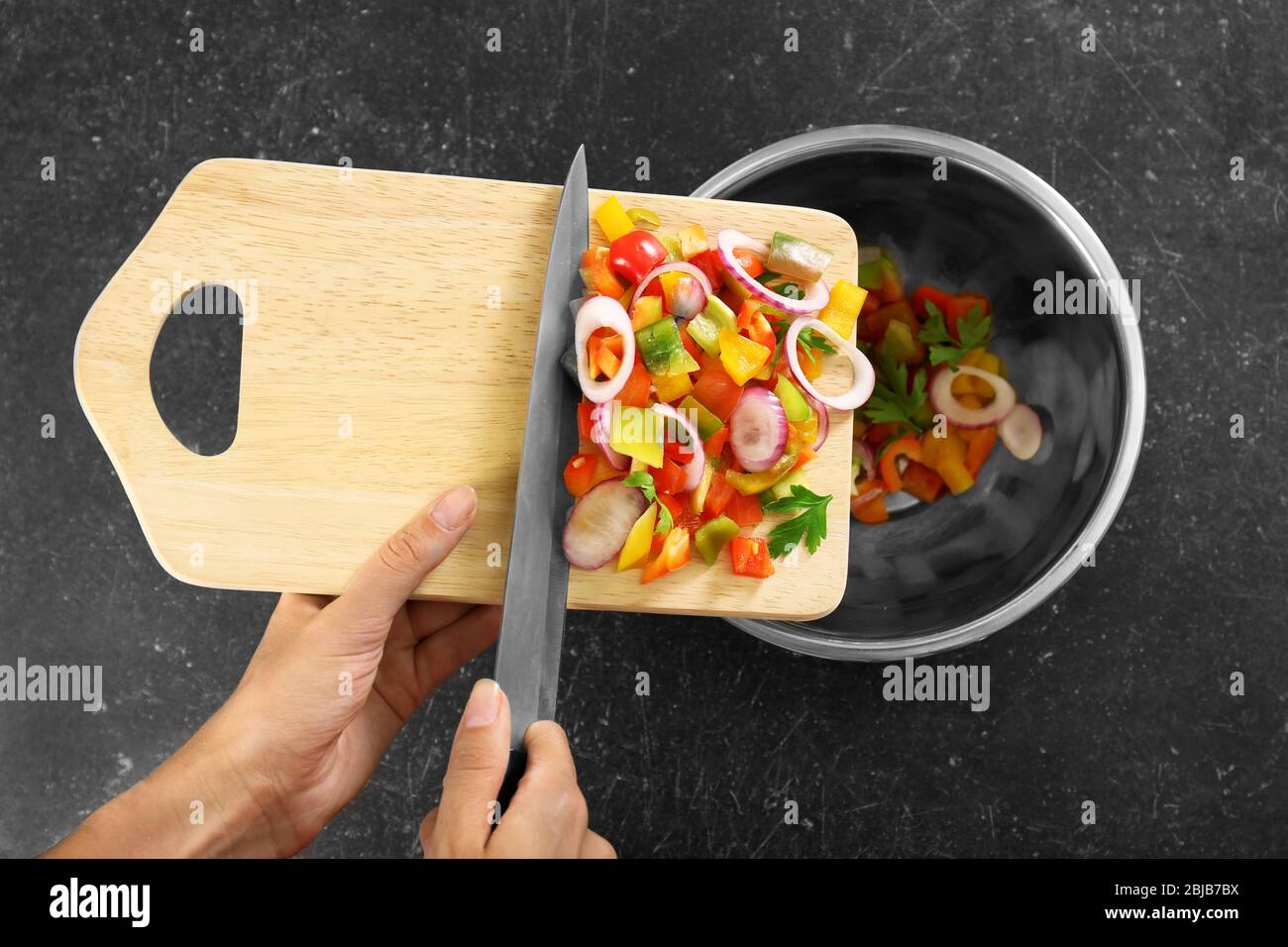 Woman putting chopped bell pepper with onion in bowl, top view Stock Photo