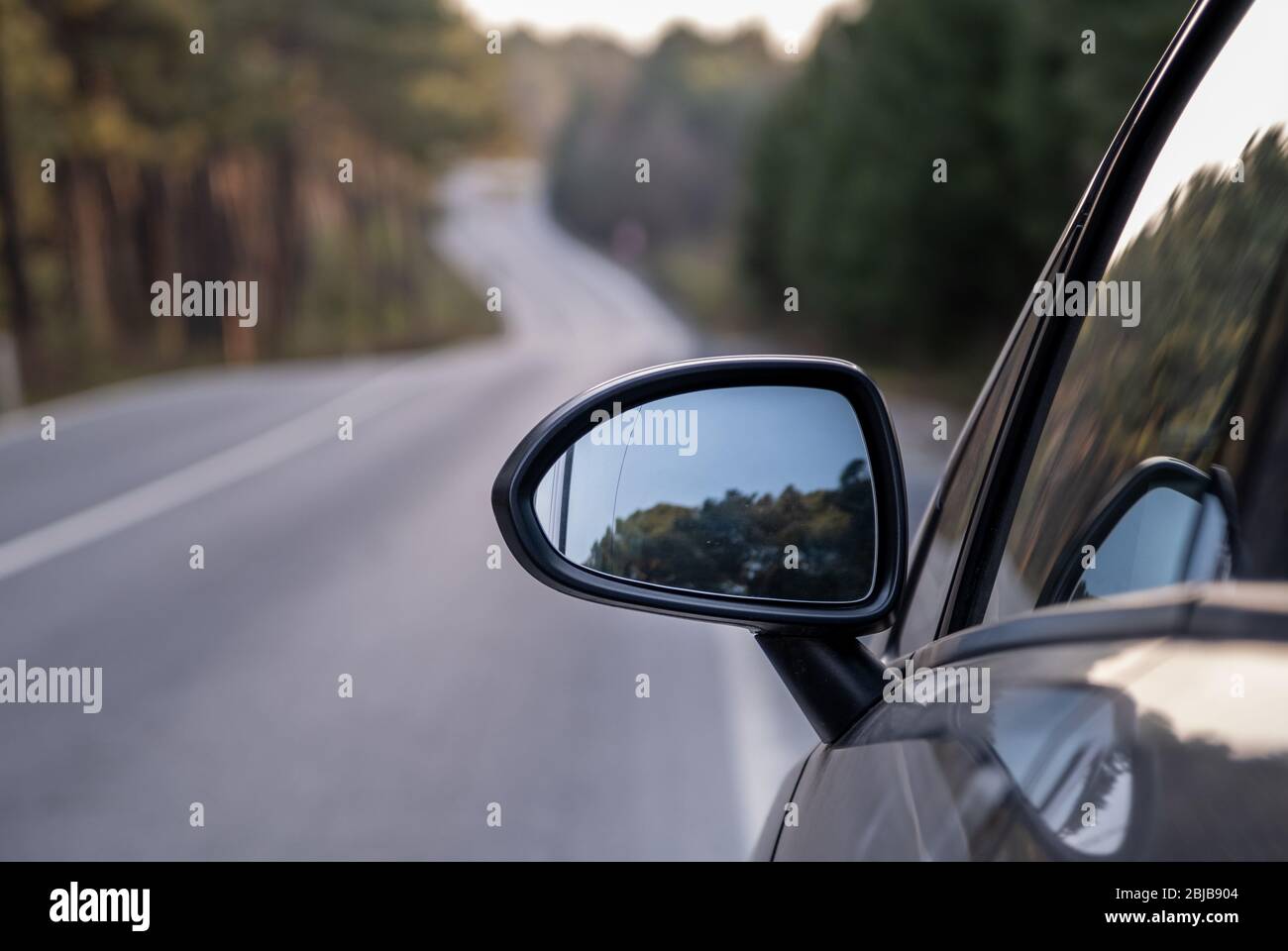 Car rear view mirror on wooded rural road Stock Photo