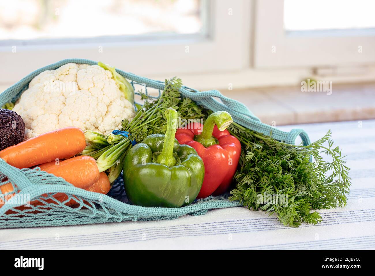 Fresh vegetables in a blue mesh bag, Reusable, sustainable, eco friendly, earth day, no plastic concept. Various vegetables: peppers, carrots, caulifl Stock Photo