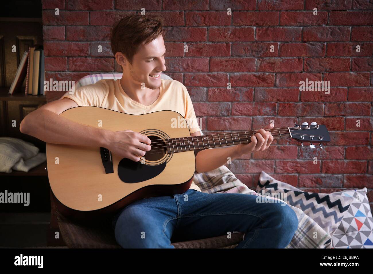 Young man playing guitar and sitting on chair in a room Stock Photo - Alamy