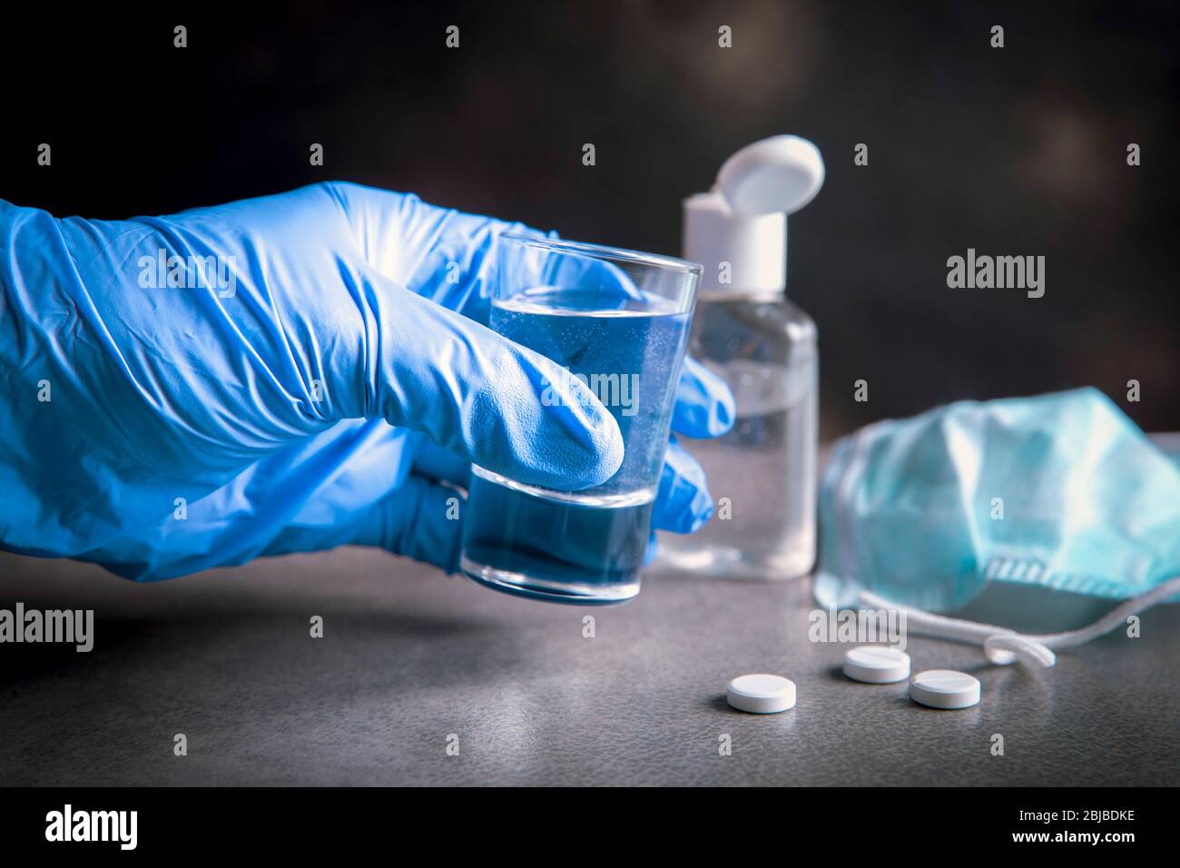 Drinking problem alcoholism during coronavirus isolation quarantine time concept. Hand with medical glove holding shot with alcohol drink. Pills, hand Stock Photo