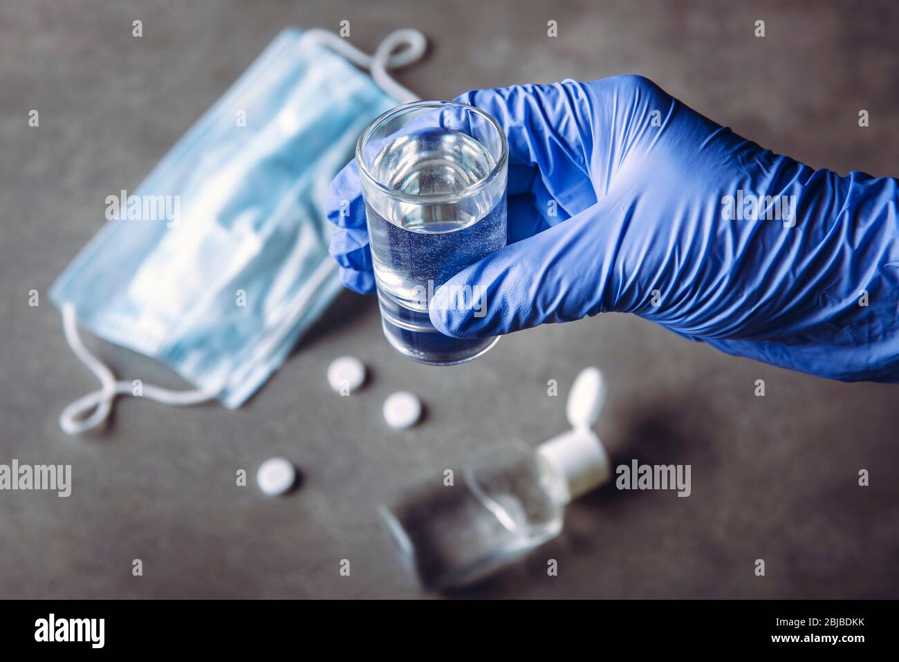 Drinking problem alcoholism during coronavirus isolation quarantine time concept. Hand with medical glove holding shot with alcohol drink. Pills, hand Stock Photo