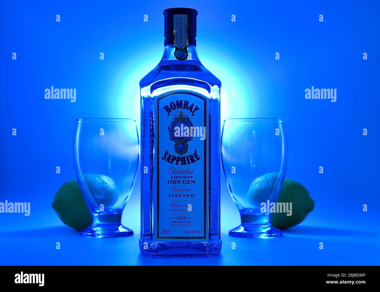 Bottle of Bombay Sapphire gin with goblets and lemons blue background Stock Photo