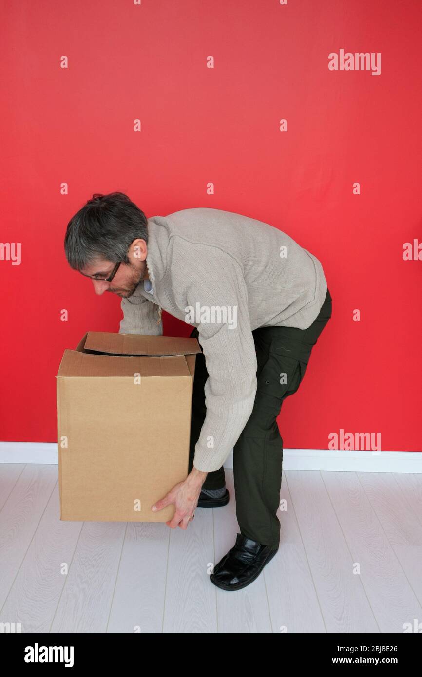 Male bending his knees to lift a heavy box Stock Photo