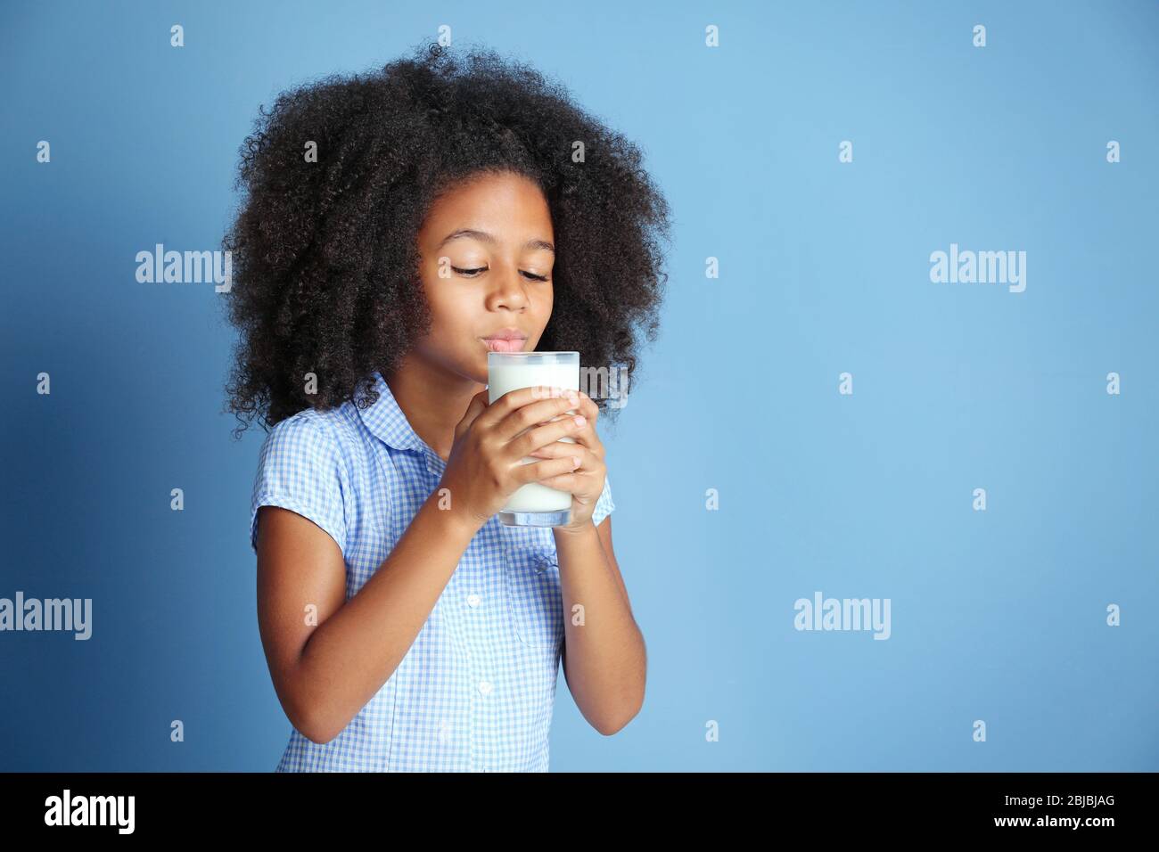 Cute curly African-American girl drinking milk on a blue background Stock Photo