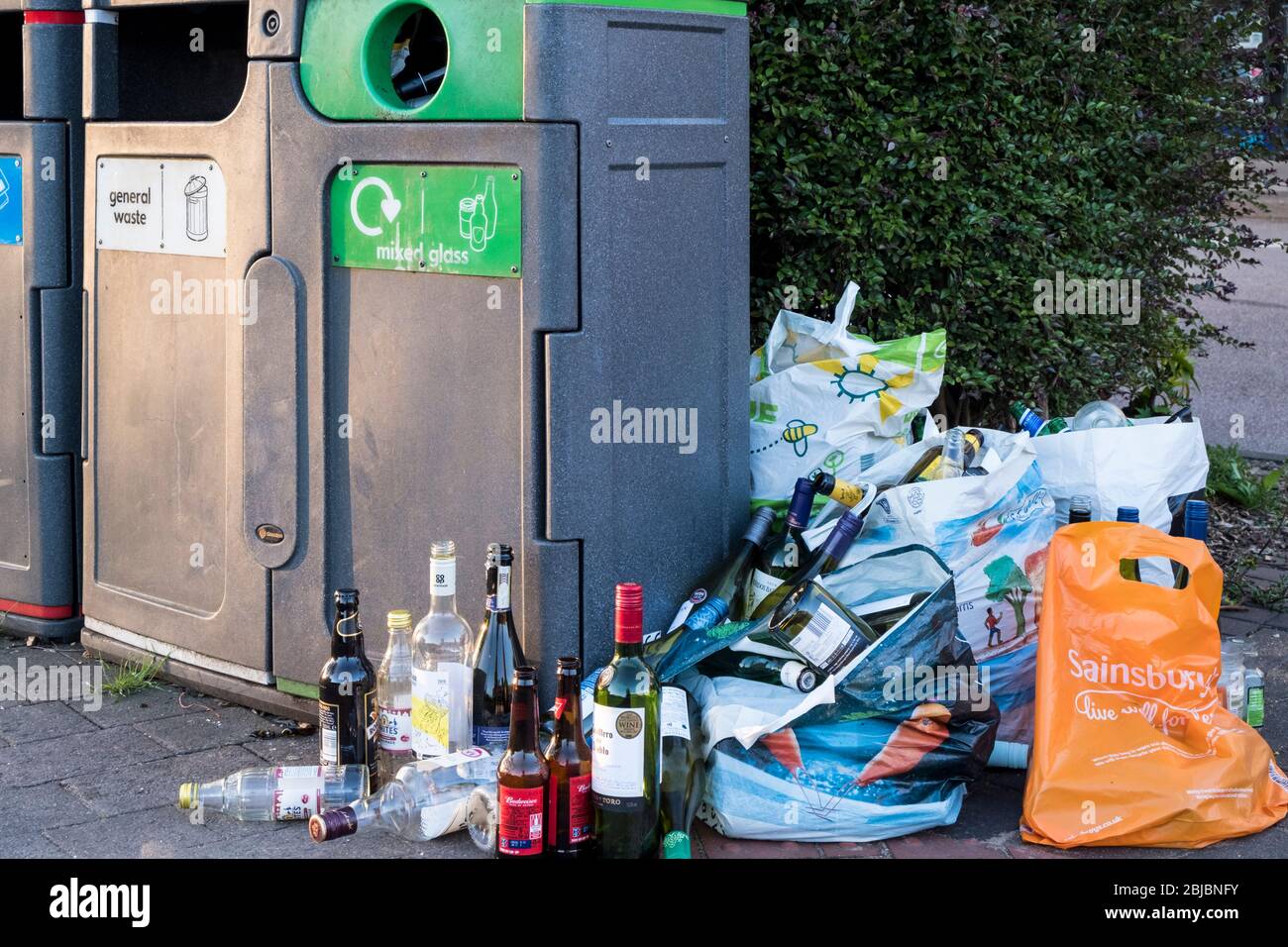 Bags of glass bottles next to a full waste recycling bin, West Bridgford, Nottinghamshire, England, UK Stock Photo