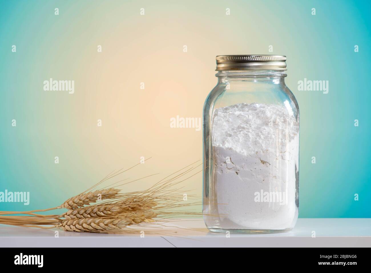 White flour in a glass jar and wheat sheaf with modern clean blue