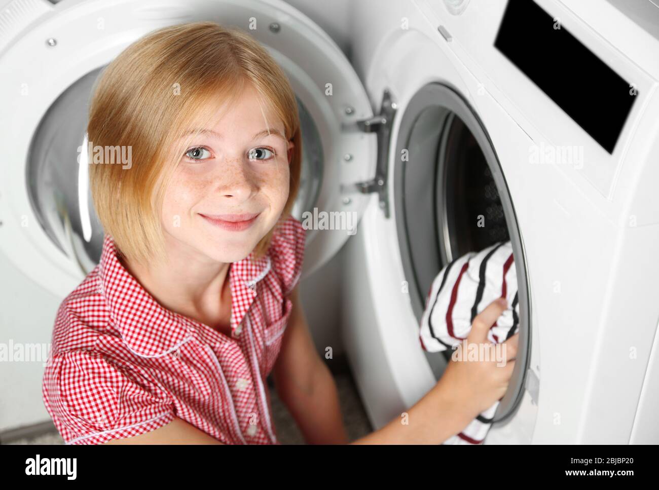 Small girl putting cloth into washing machine Stock Photo