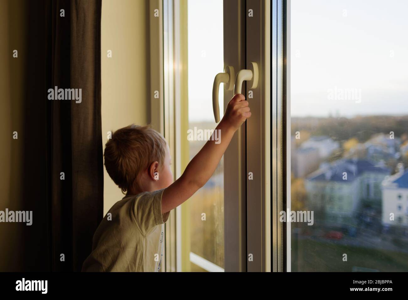 Child opening window without parents, holding handle. Dangerous situation Stock Photo