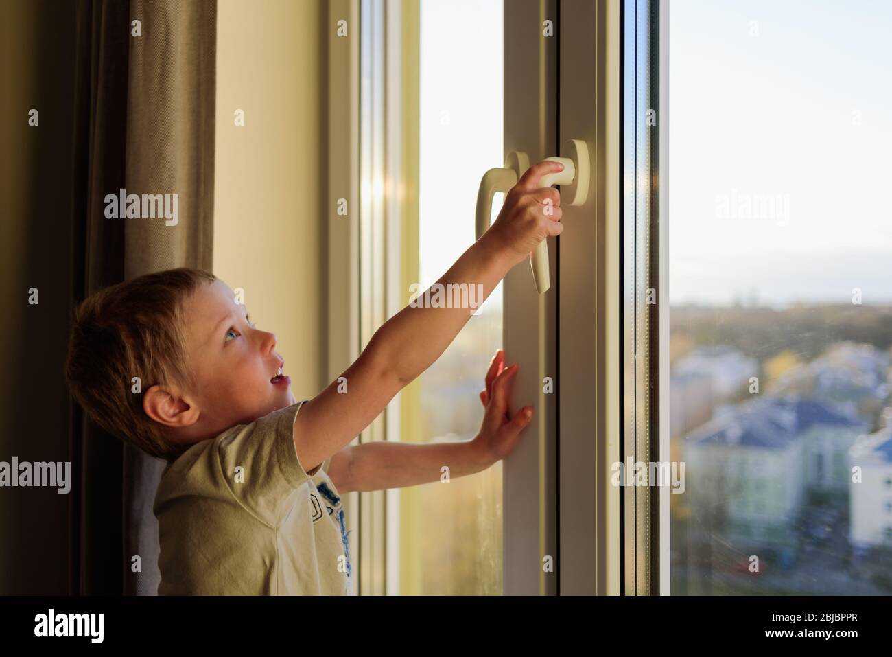 Child opening window without parents, holding handle. Dangerous situation Stock Photo