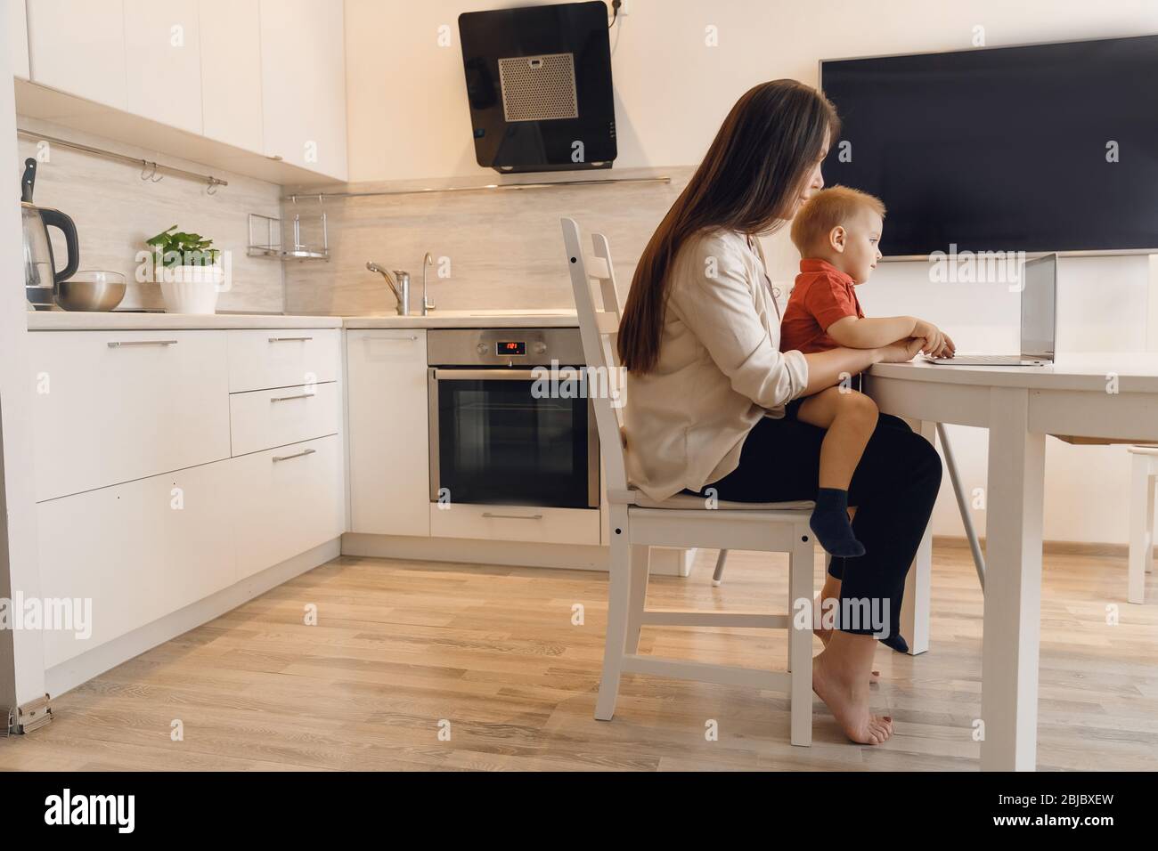 Business mom is using online work laptop, woman spending time with her boy baby home Stock Photo