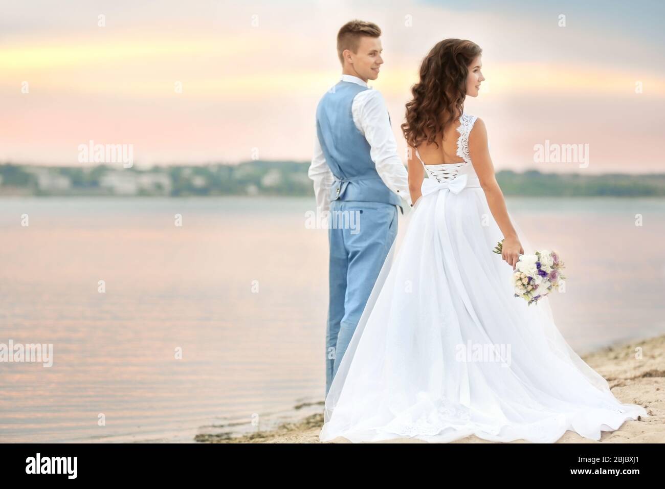 Beautiful wedding couple walking along riverside Stock Photo - Alamy