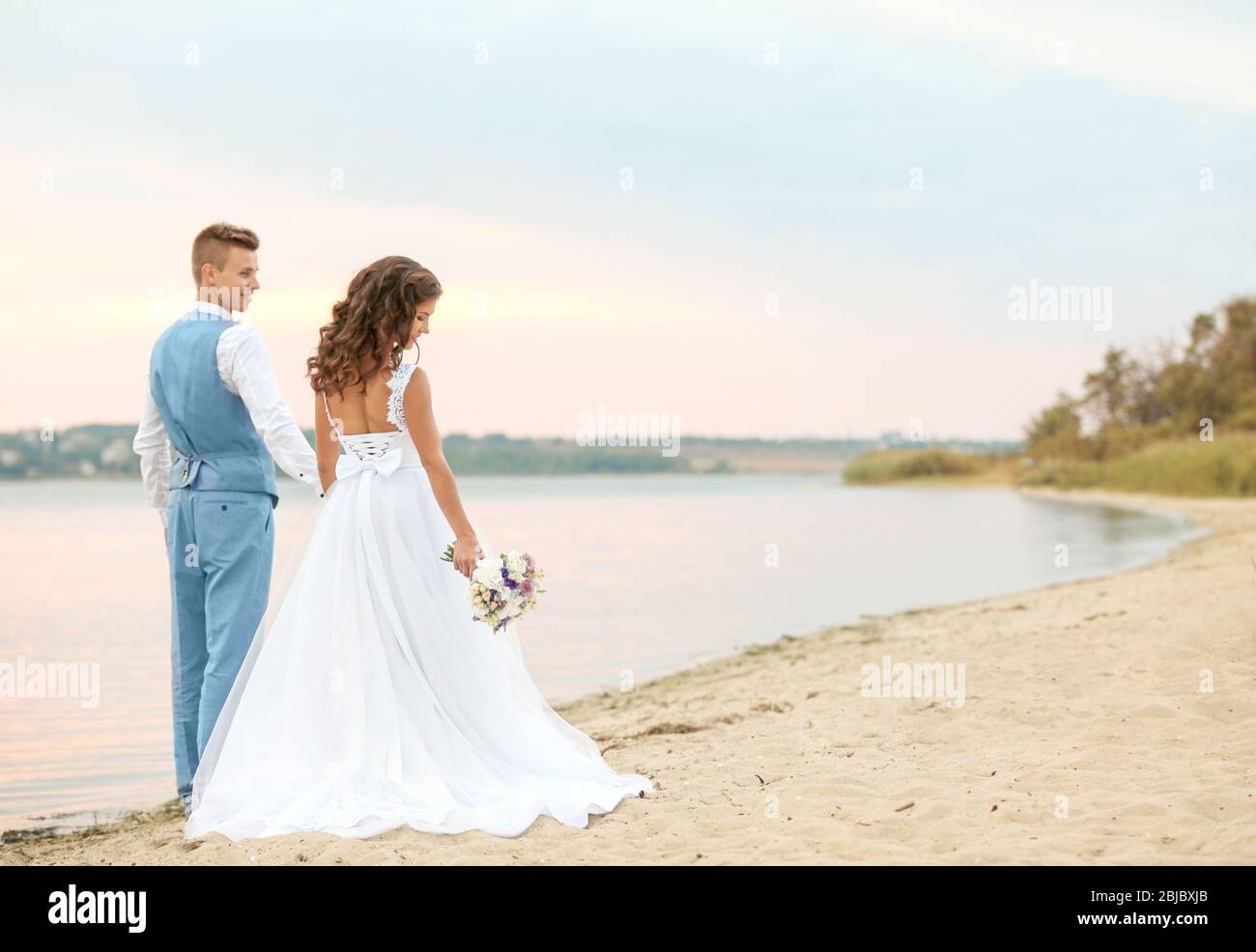 Beautiful wedding couple walking along riverside Stock Photo - Alamy