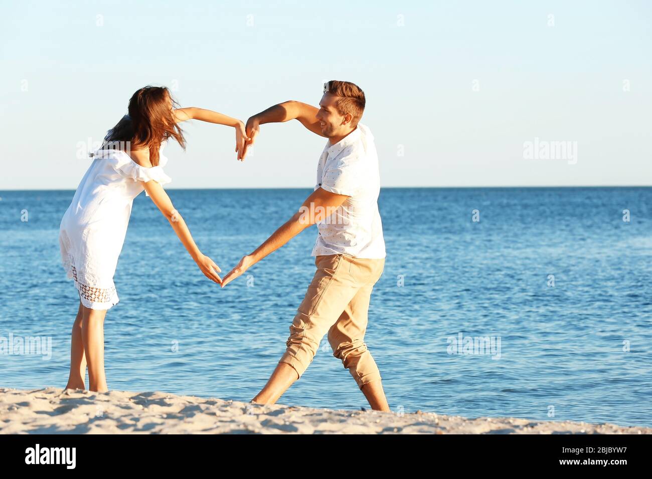 Young couple making heart with their hands on beach Stock Photo - Alamy