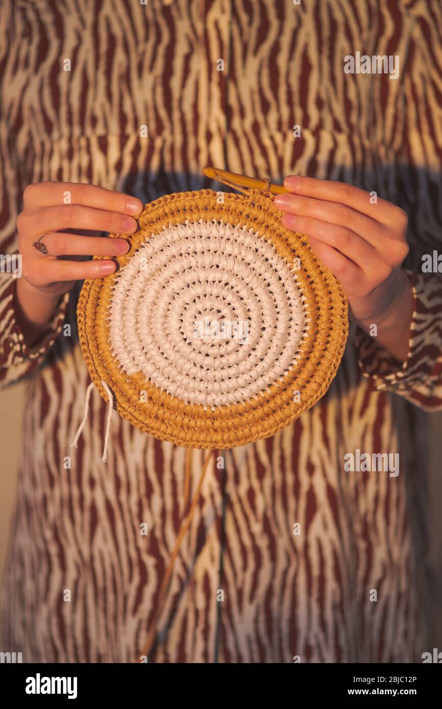 Round raffia crochet panno in female hands. Handcraft, hobby concept: holding a wall hanging and a crochet hook Stock Photo