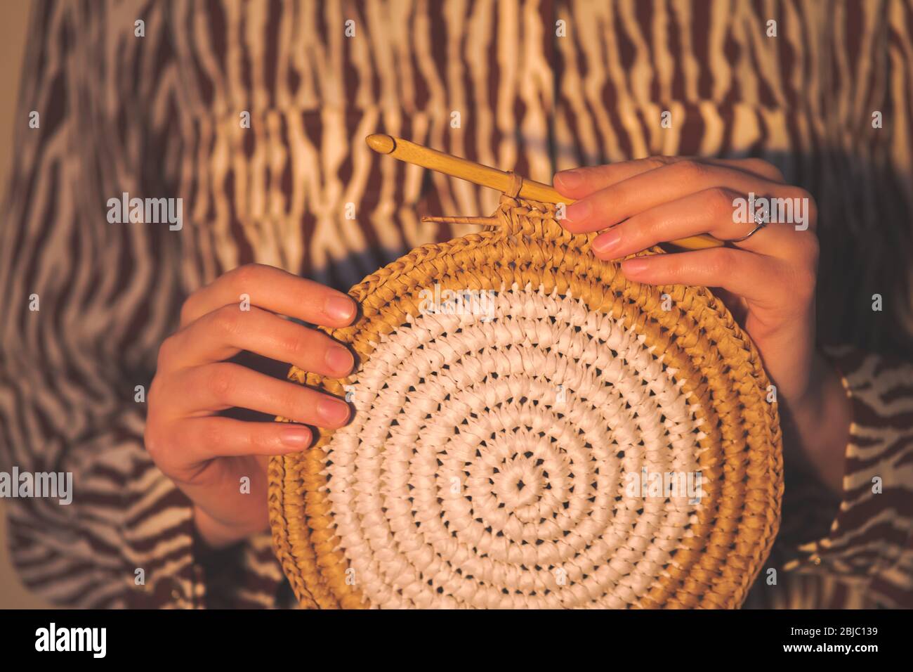 Round raffia crochet panno in female hands. Handcraft, hobby concept: holding a wall hanging and a crochet hook Stock Photo