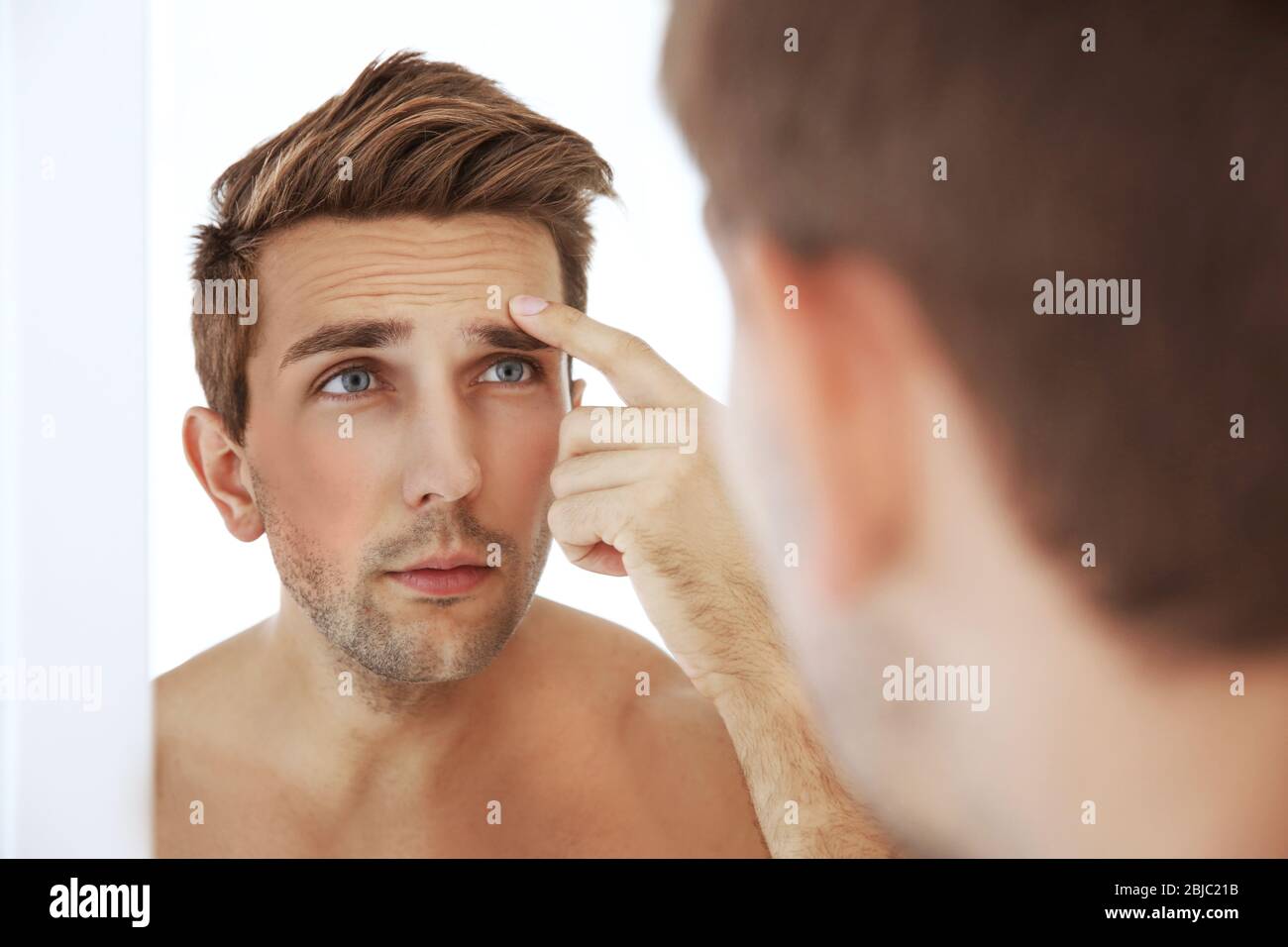 Young man standing in front of mirror and touching his face Stock Photo
