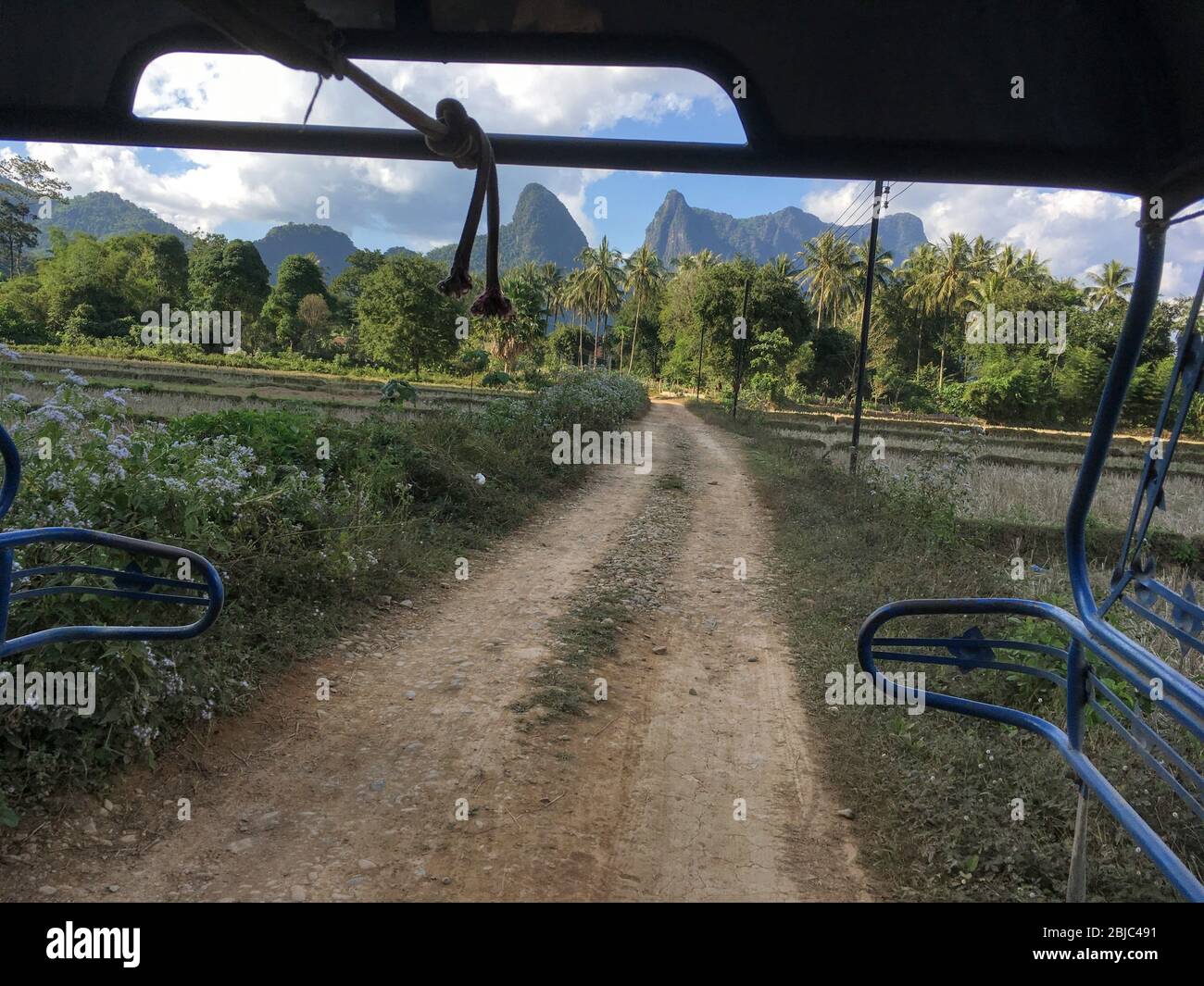 View of Unpaved Road and Tropical Jungle Mountain from Tuk Tuk truck, Vang Vieng, Laos Republic Stock Photo
