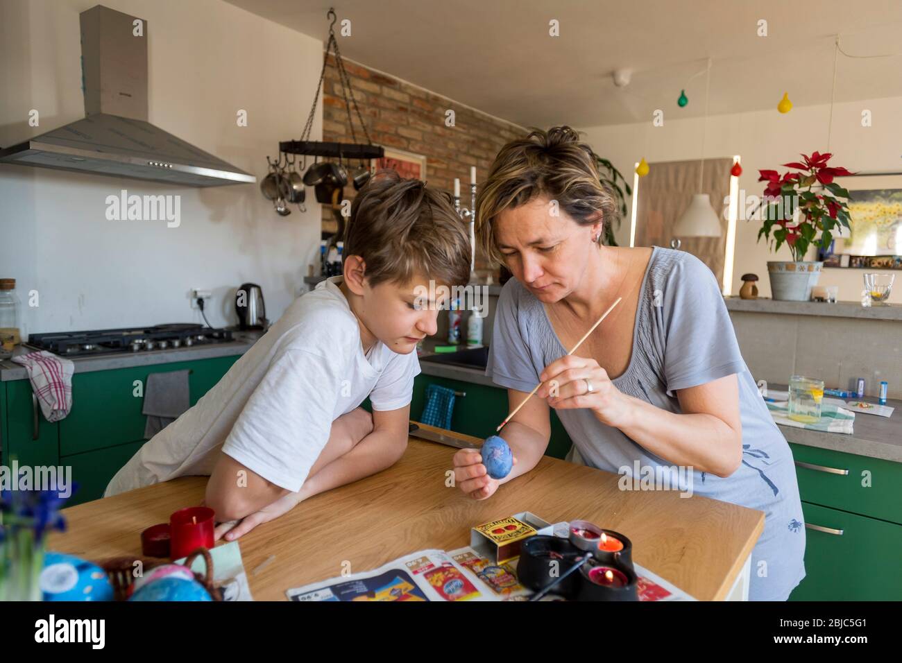 mother and son colouring Easter egg at home in the kitchen Stock Photo