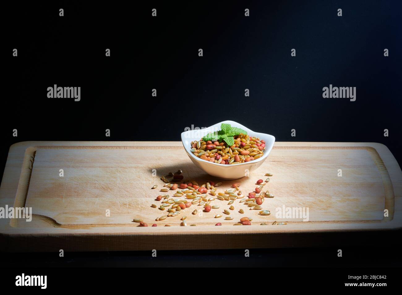 Beans and rye with mint leaves on a white bowl, on a wooden chopping board, illuminated by direct sunlight Stock Photo