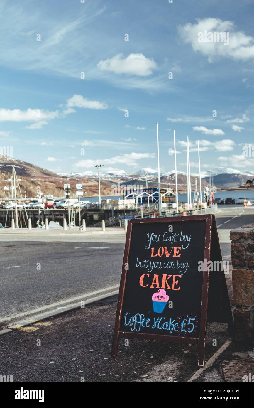 "You can't buy love, but you can buy cake" announcement written on a chalk blackboard, attracting customers to the local cafe in Ullapool village in S Stock Photo