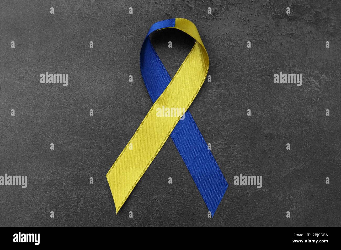 Blue-and-yellow ribbon on dark background. Down syndrome concept Stock