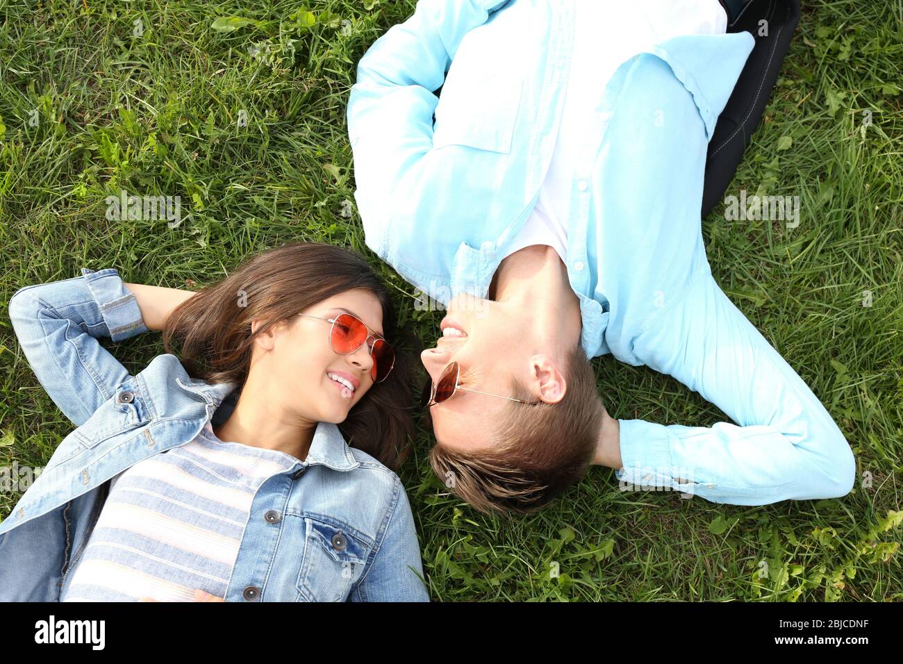 Beautiful young couple lying on green grass Stock Photo - Alamy